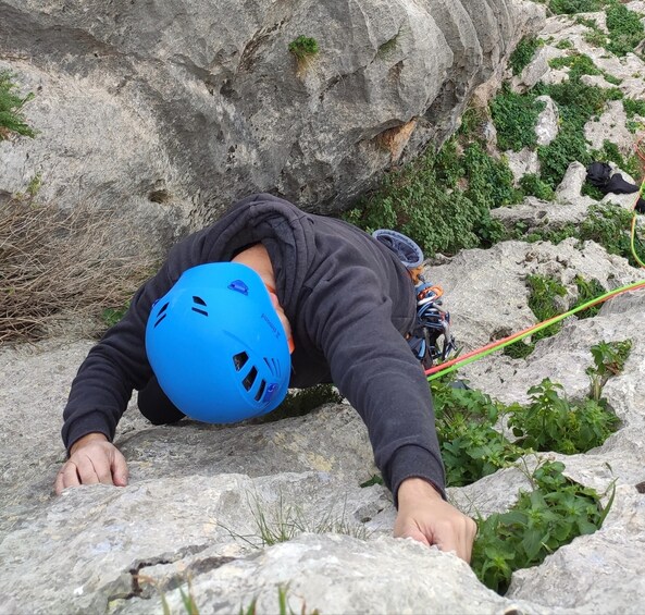 A person climbing a rocky terrain with a blue helmet and climbing gear. 3