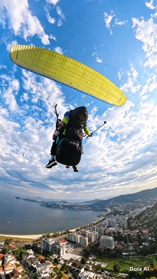 A paraglider with a yellow canopy flying over a coastal city with a view of the sea and mountains in the background. 3