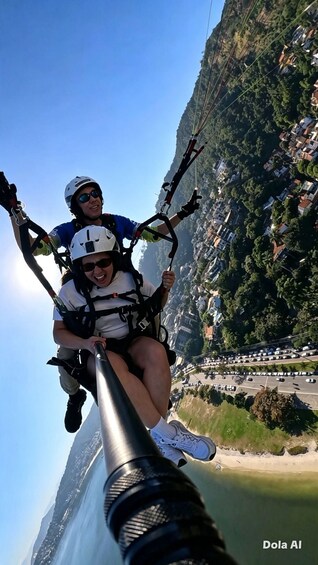 Two people on a tandem paragliding flight, with a mountainous landscape and a coastal road in the background. 4