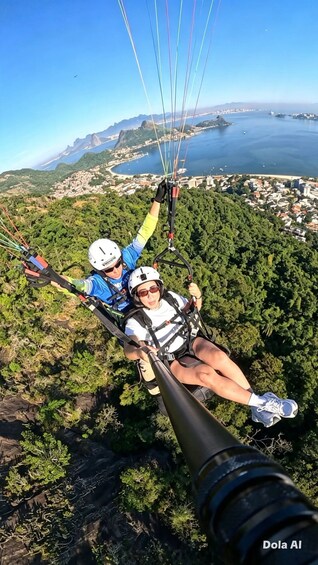 Two people paragliding over a coastal landscape with mountains and a body of water in the background. 1