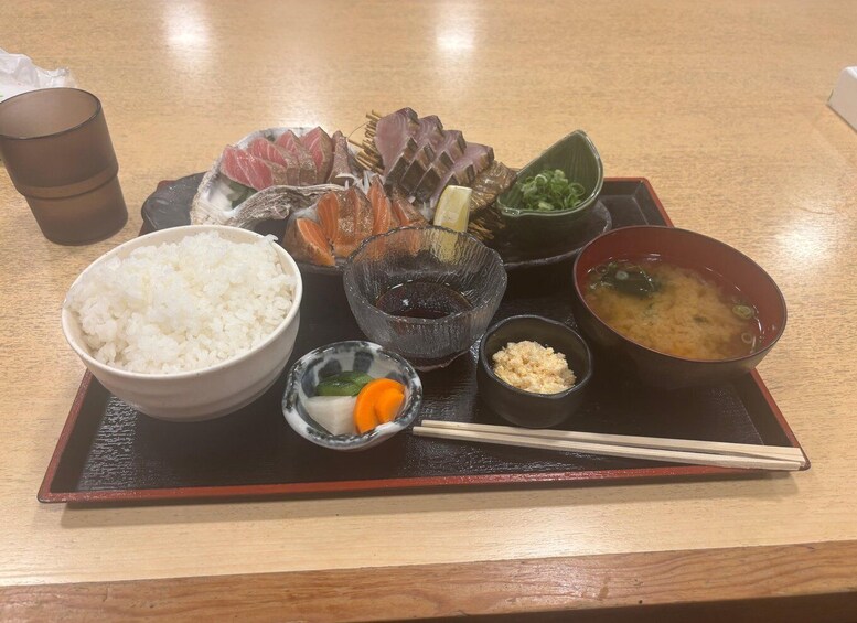 A Japanese meal with rice, soup, and various sashimi on a black tray. 3