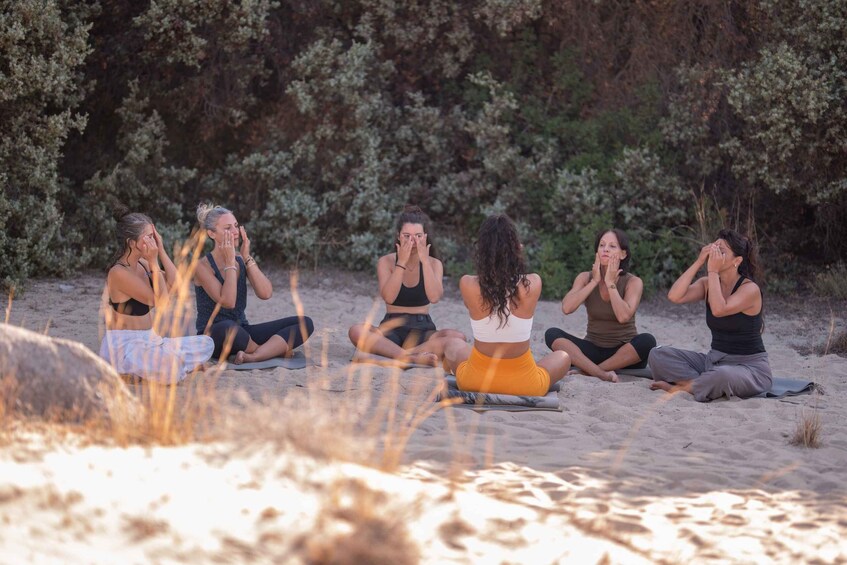 A group of people sitting on the beach in a circle, some with their hands on their faces. 4