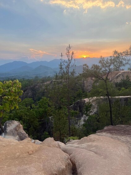 A mountainous landscape with a sunset, rocky outcrops, and sparse vegetation. 4
