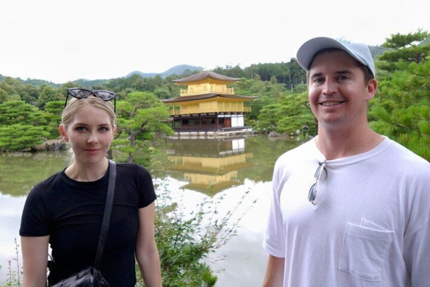 A person standing in front of a traditional building with a reflection in the water. 1