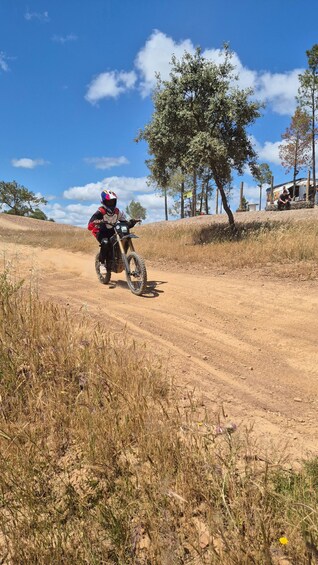 A person riding a dirt bike on a dirt path with sparse vegetation and a clear blue sky. 3