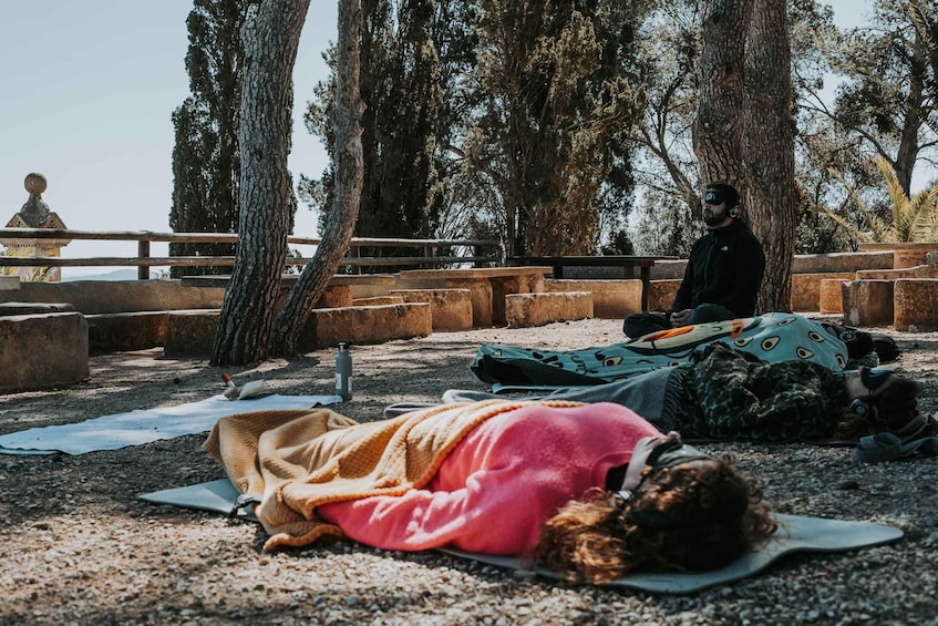A person meditating on a mat in a park with trees and a stone bench. 1