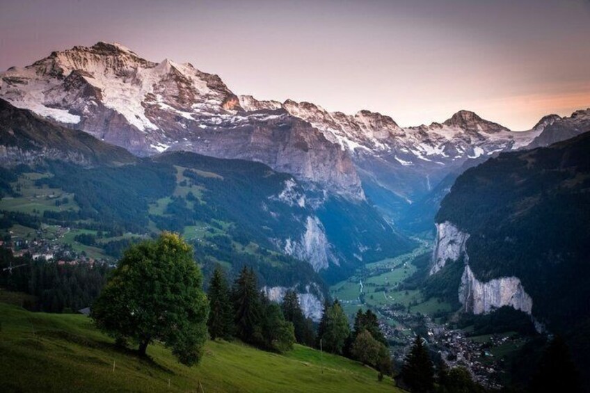 A mountainous landscape with snow-capped peaks, a valley, and a small settlement. 1