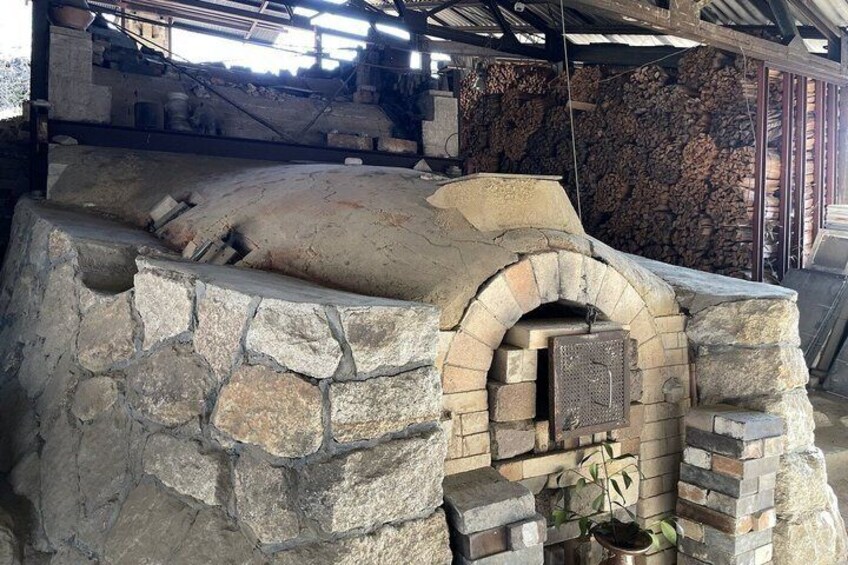 A stone-built outdoor oven with a brick archway, surrounded by stacked firewood and a metal structure overhead. 5