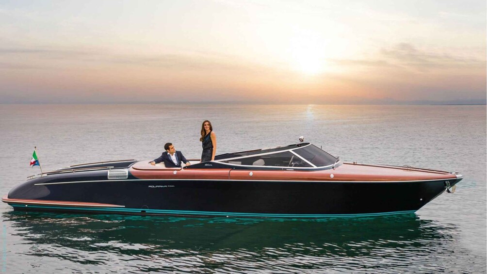 A sleek, modern boat with a red and black color scheme, a flag, and two people on board. 1