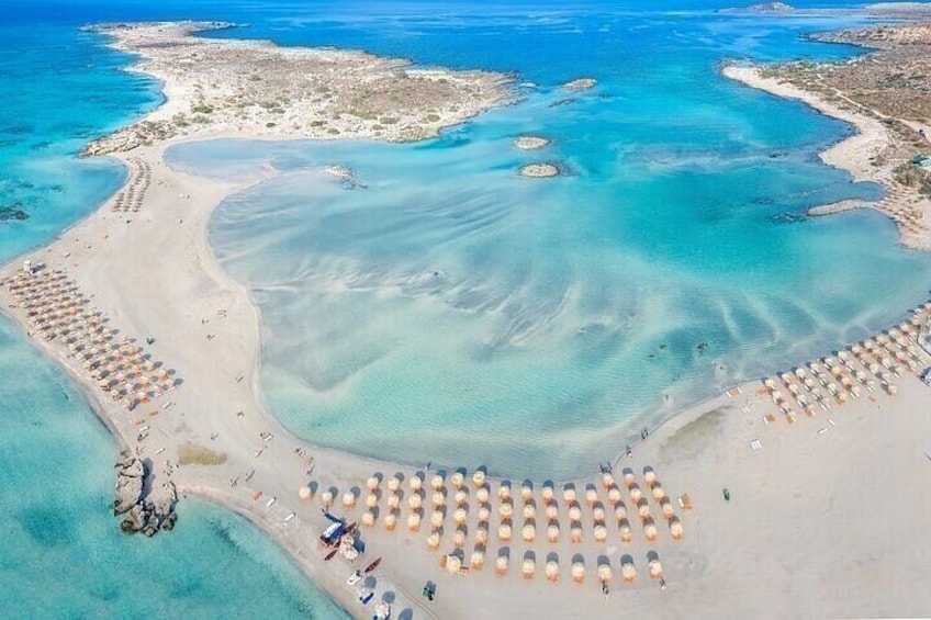 An aerial view of a beach with clear turquoise waters, a sandy shore, and rows of sun loungers. 2