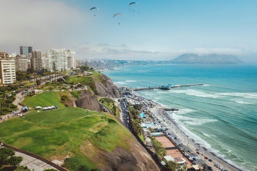 A coastal cityscape with buildings, a beach, and a cliff overlooking the ocean. 1