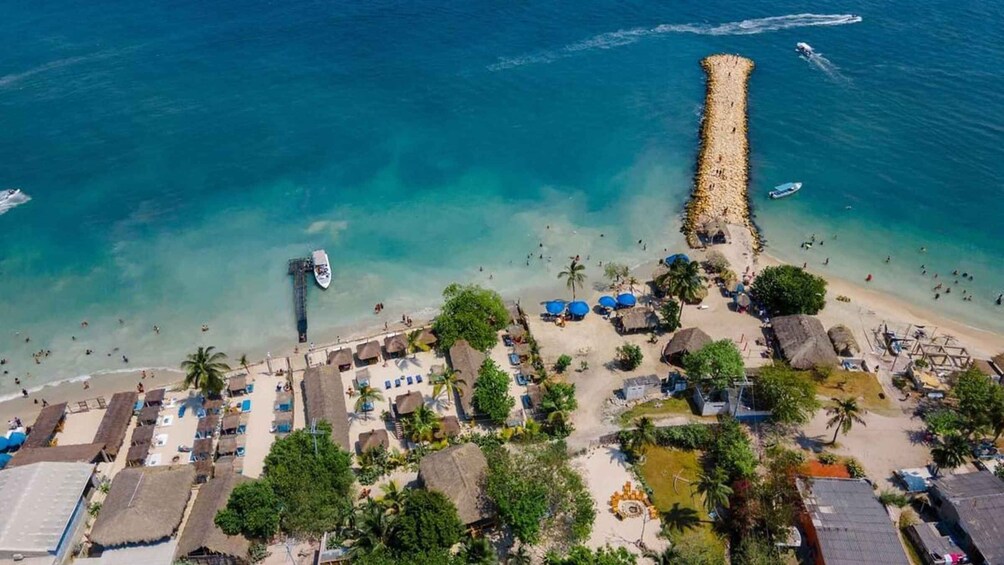 An aerial view of a beach with a pier extending into the sea, surrounded by thatched-roof huts and palm trees. 3