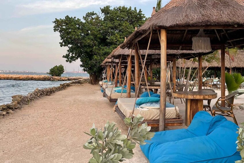 A beachside lounge with thatched-roof structures, blue cushions, and a view of the sea. 1