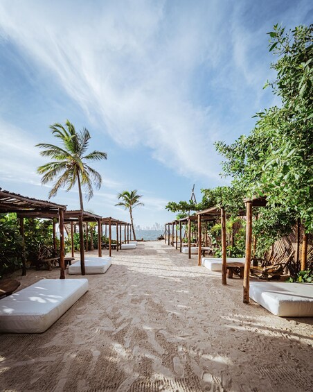 A beach with wooden gazebos and white lounge chairs, palm trees, and a clear sky. 5