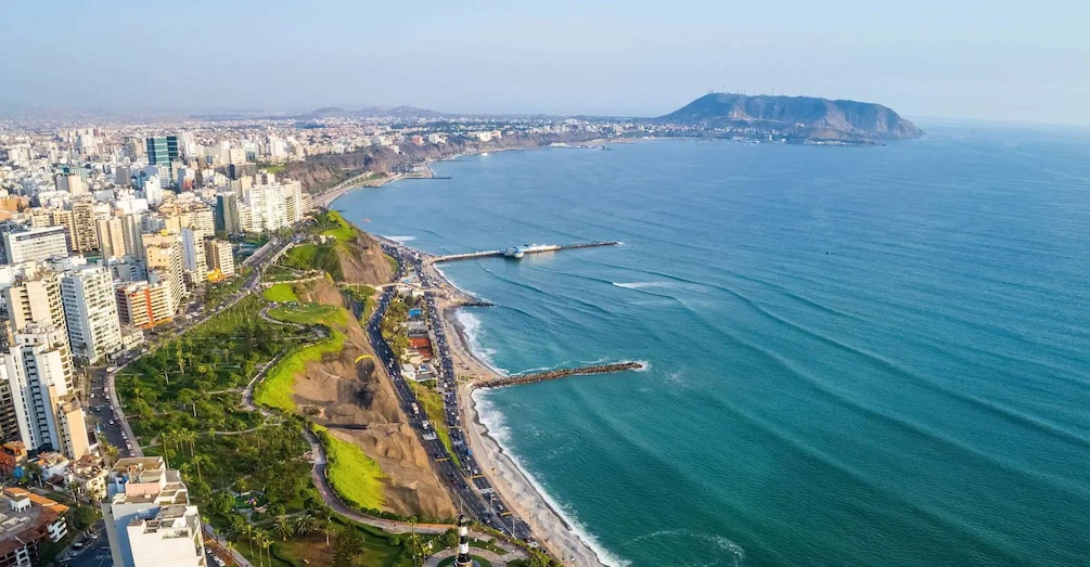 A coastal cityscape with high-rise buildings, a beach, and a prominent hill in the distance. 1