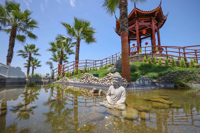 A serene pond with a Buddha statue, palm trees, and a traditional red pavilion. 2