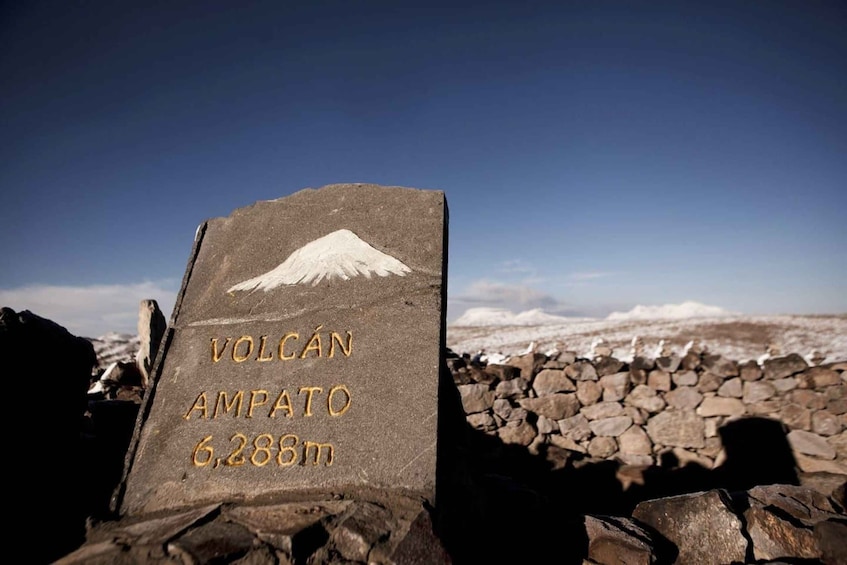 A stone marker with 'Volcán Ampato 6,288m' inscribed, set against a snowy landscape. 4