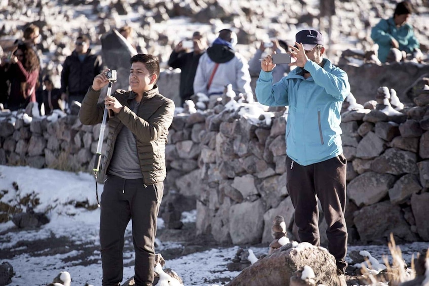 Two individuals taking photographs in a rocky outdoor setting with snow on the ground. 3