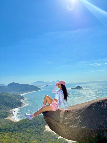 A person sitting on a rock overlooking a coastal landscape with mountains and the ocean. 3