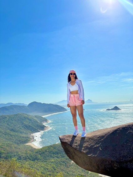 A person standing on a rock overlooking a coastal landscape with mountains and the ocean. 1