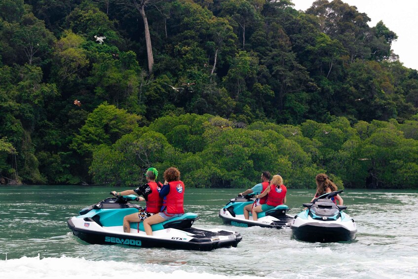 Four people on jet skis on a river surrounded by dense forest. 1