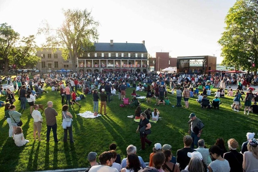 A large outdoor gathering on a grassy field with a building in the background. 2