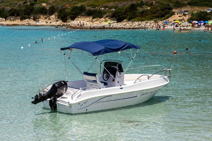 A white motorboat with a blue canopy docked near a beach with people swimming and umbrellas in the background. 3