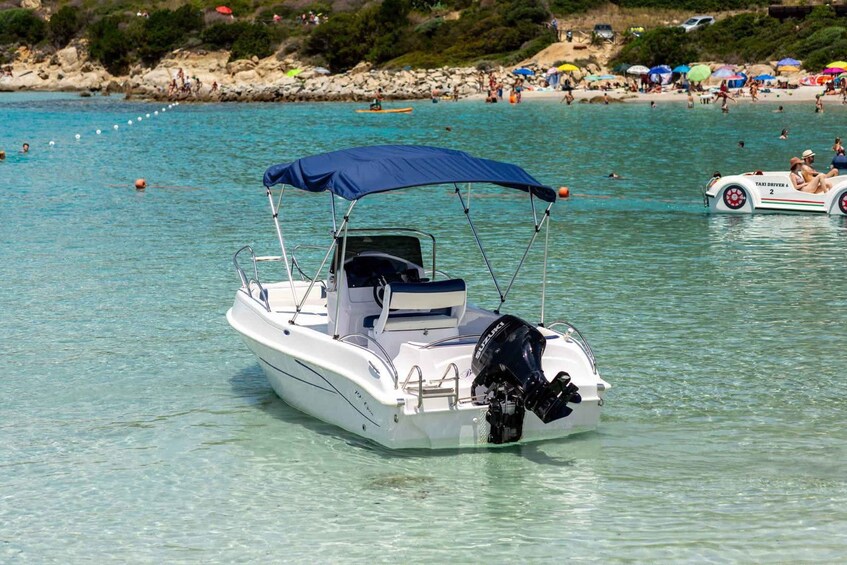 A white boat with a blue canopy anchored near a beach with people and umbrellas. 2