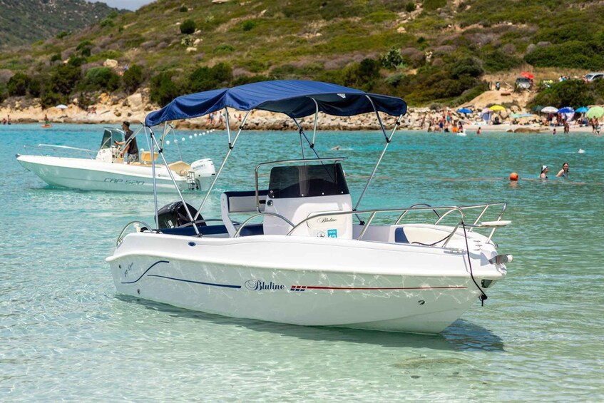 A boat named 'Bluline' anchored near a beach with people swimming and umbrellas in the background. 1