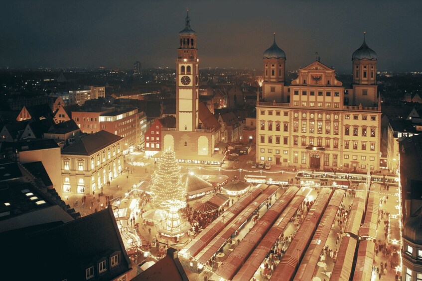 A cityscape with a prominent clock tower, a large Christmas tree, and a market area with tents. 5