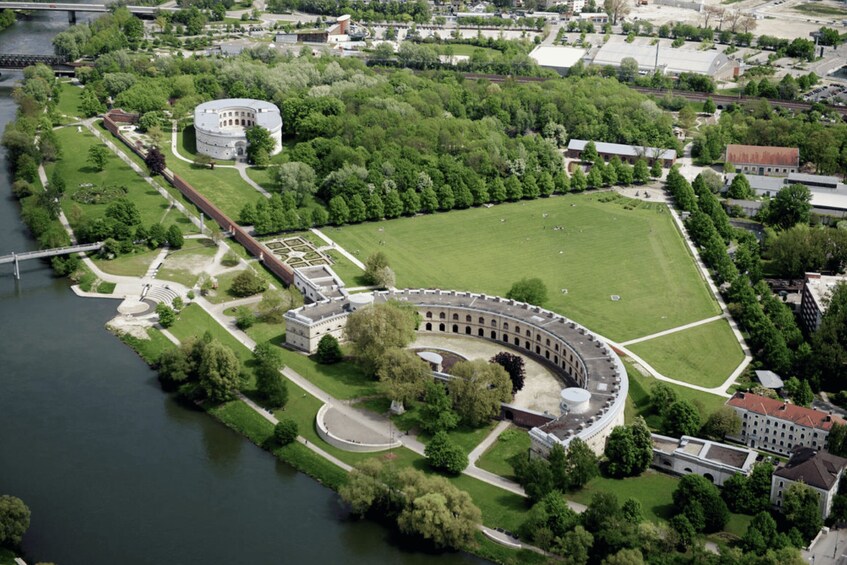An aerial view of a historic circular building with a surrounding park and river. 2