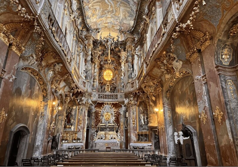 An ornate church interior with detailed frescoes, a central altar, and a large chandelier. 4