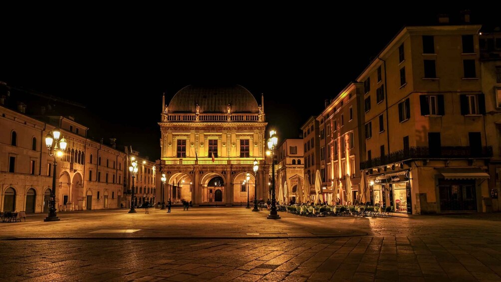A historic square with a prominent building featuring a dome and classical architecture, illuminated by street lamps. 2