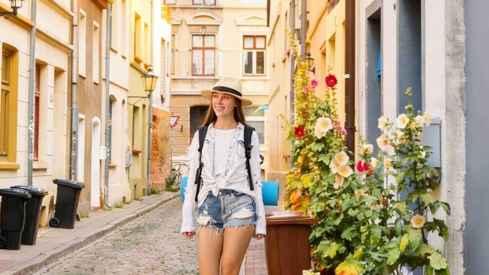 A person walking down a cobblestone street lined with buildings and flowering plants. 4