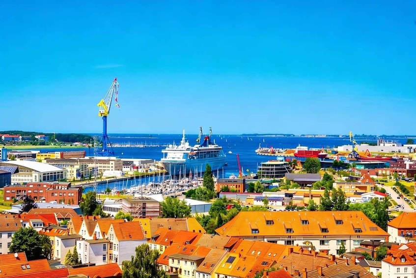 A coastal cityscape with a prominent blue crane, a large cruise ship docked, and a marina filled with boats. 1