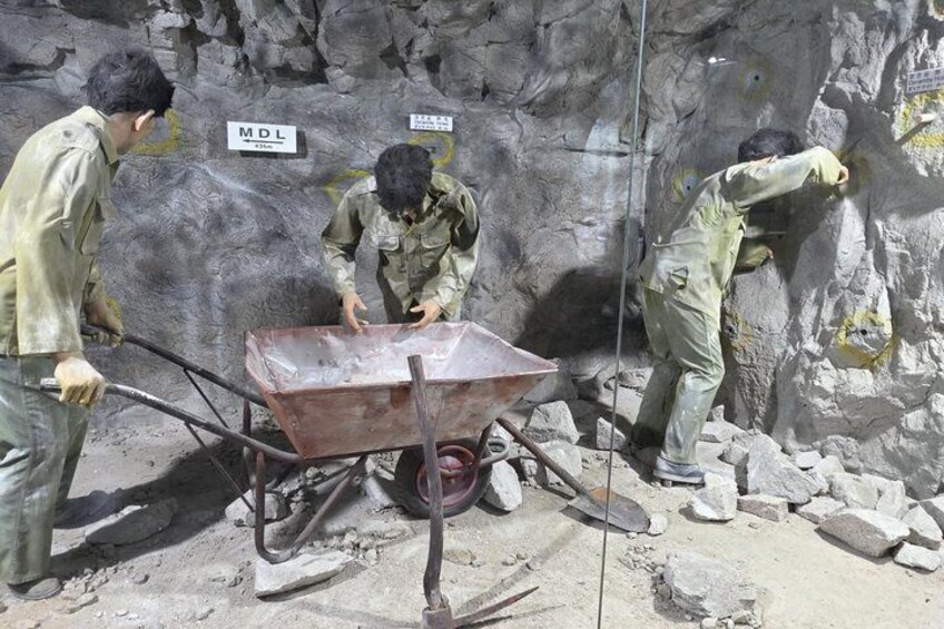 Three workers in a mining area with a wheelbarrow and a sign that reads 'MDL.' 4