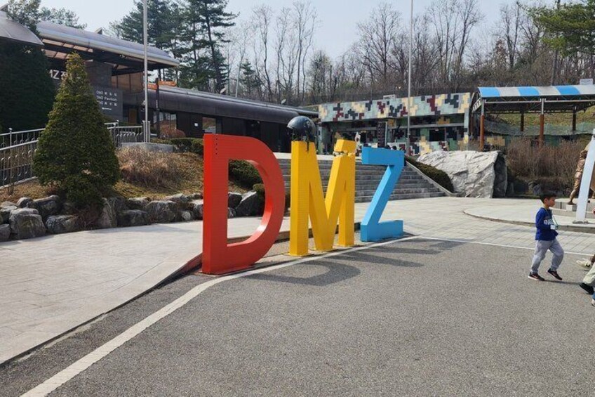 Large colorful letters 'DMZ' in a parking lot with a building in the background. 2