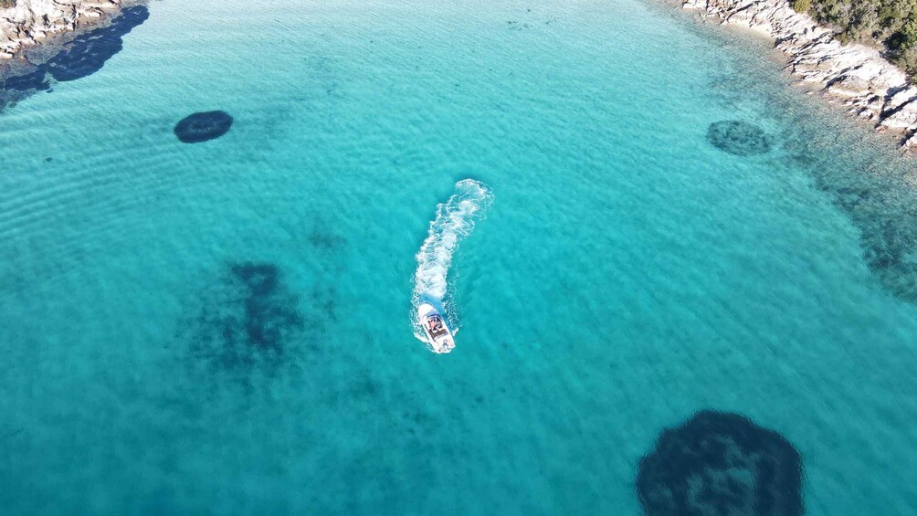 A boat moving through clear turquoise water with rocky shores and visible underwater formations. 1