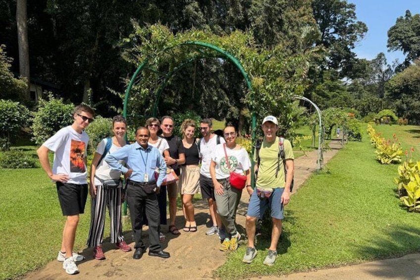 A group of people standing in a park with a green archway and lush greenery in the background. 1