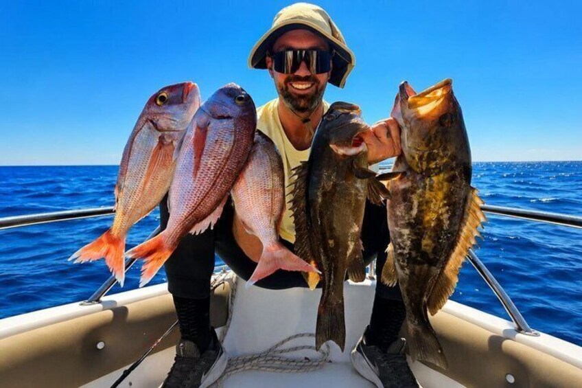 A person holding three fish on a boat with the ocean in the background. 1