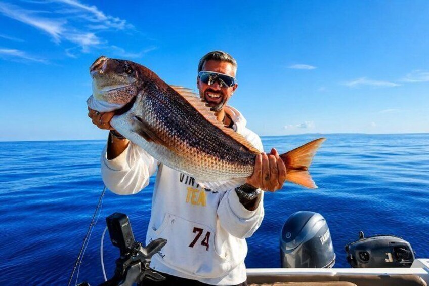 A person holding a large fish on a boat with a clear blue ocean in the background. 3