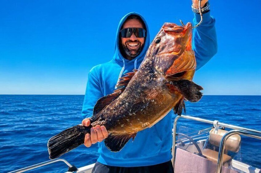 A person holding a large fish on a boat with a clear blue sky in the background. 5