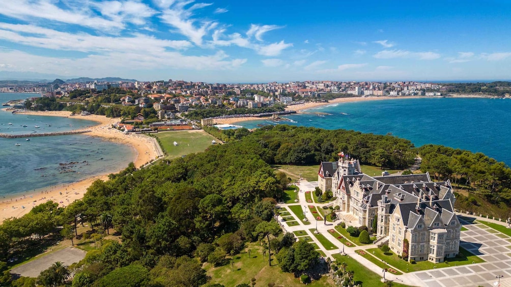 A coastal cityscape with a prominent castle, a beach, and a dense urban area in the background. 1