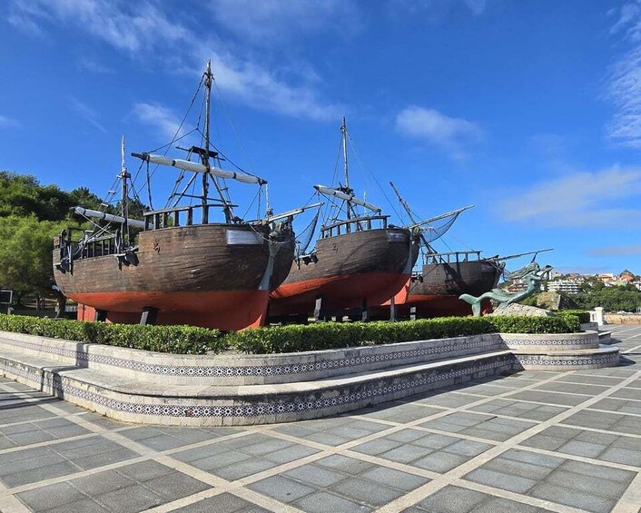 Two large wooden ships on display in a tiled plaza with a clear blue sky. 3