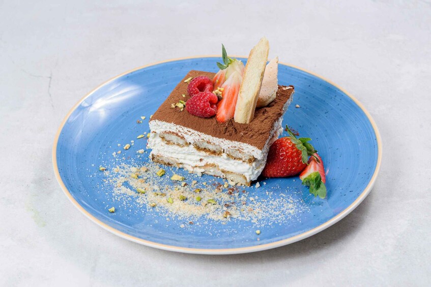 A slice of layered dessert on a blue plate with strawberries and a wafer. 3