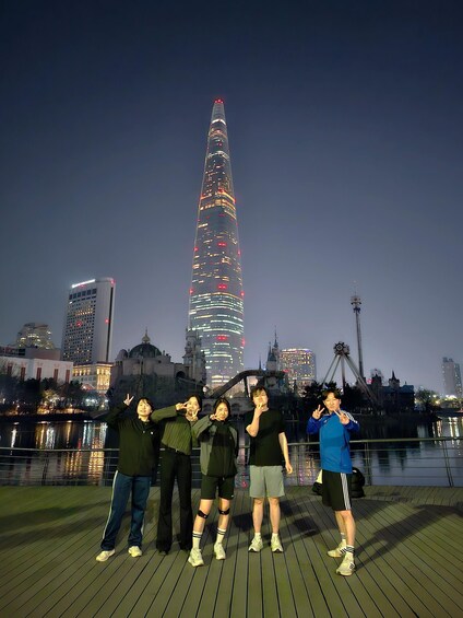 A group of people posing on a dock with a city skyline in the background, including a prominent illuminated tower. 4