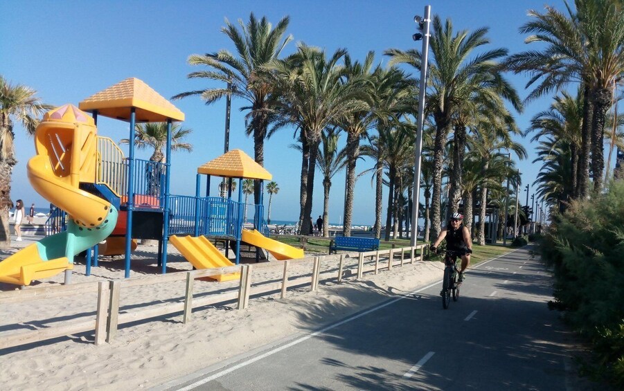 A beach playground with slides and a cyclist on a paved path. 2