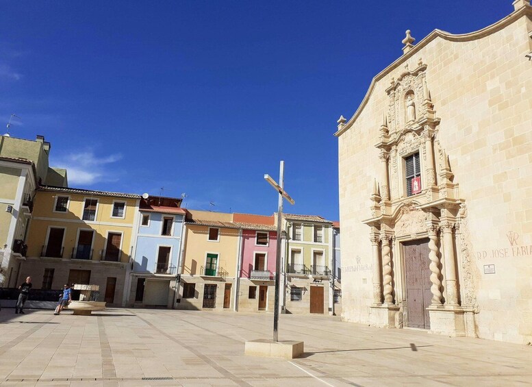 A plaza with colorful buildings, a cross, and a church with ornate architecture. 3