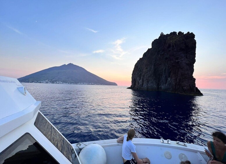 A boat with two people, a rocky outcrop, and a distant island. 1