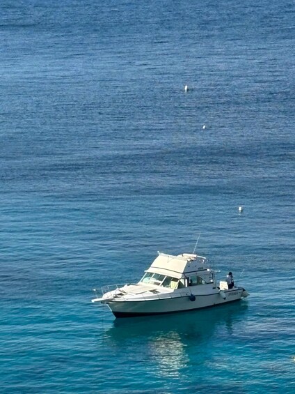 A white boat with a cabin and a person standing on the deck, floating on calm blue water. 2